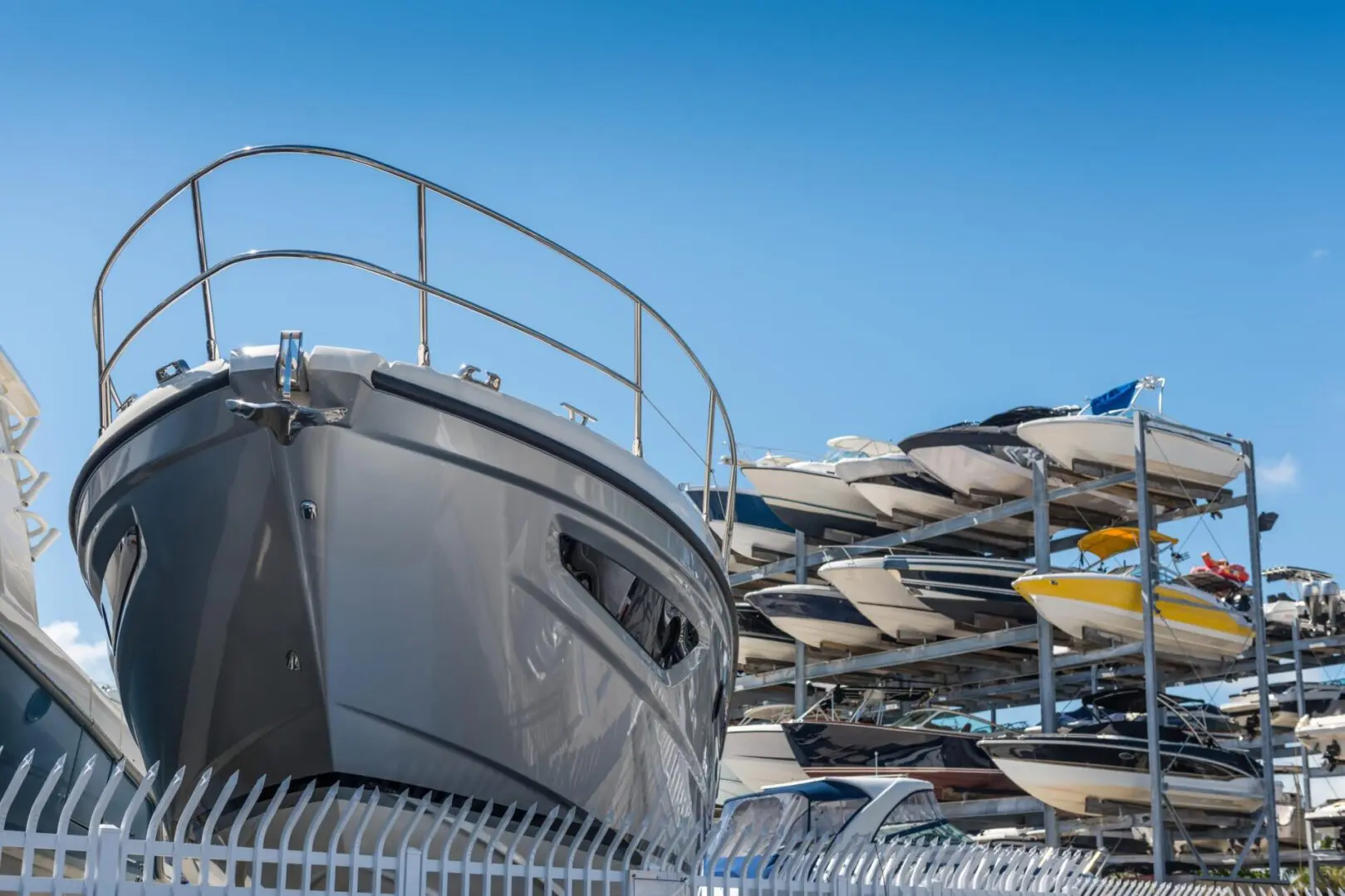 Several boats are stored on metal racks above a fenced area under a clear blue sky.